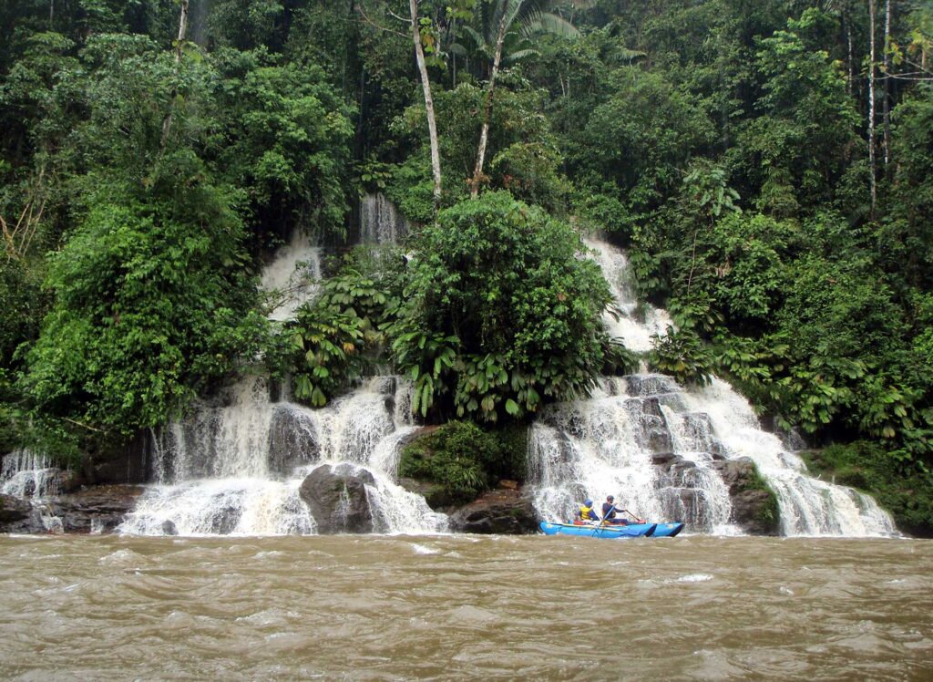 Travelers kayaking by a jungle waterfall in the Amazon rainforest